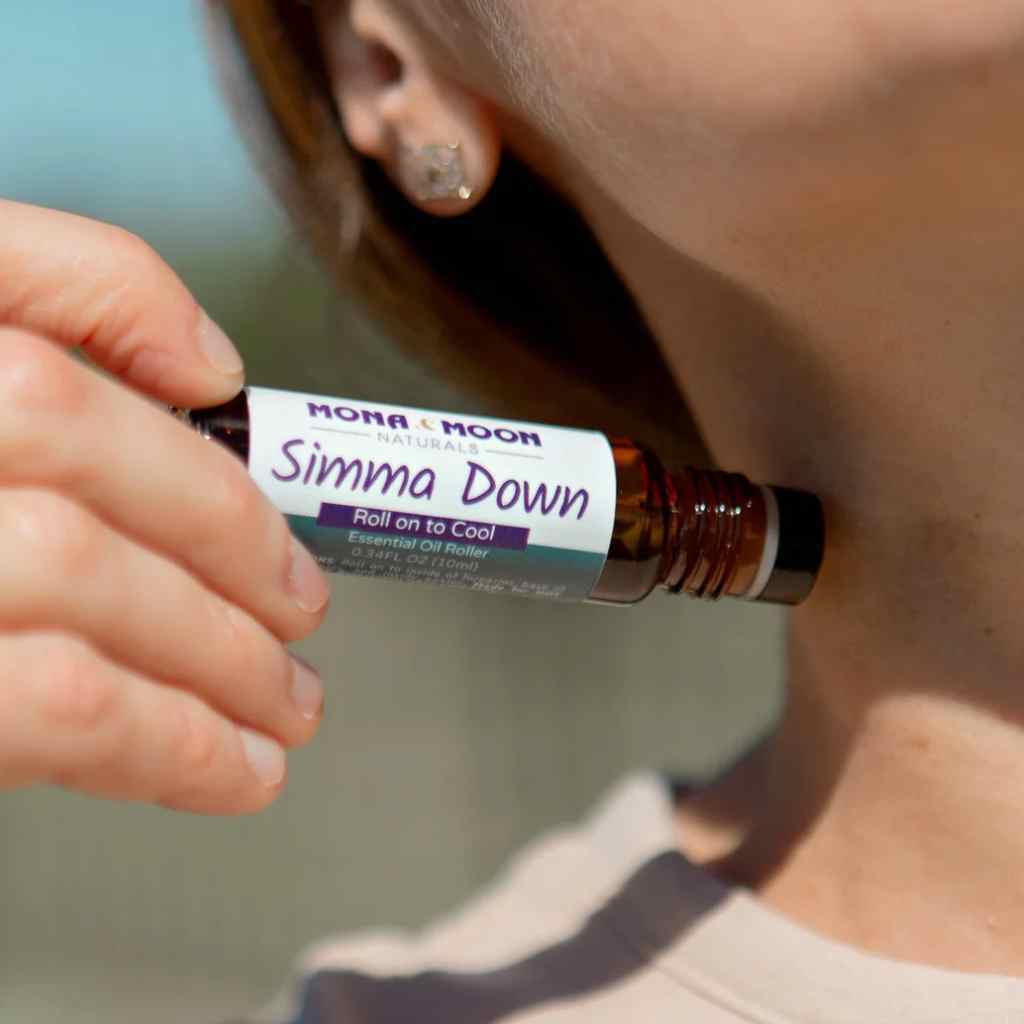 Person holding a bottle labeled 'Simma Down' near their neck outdoors.