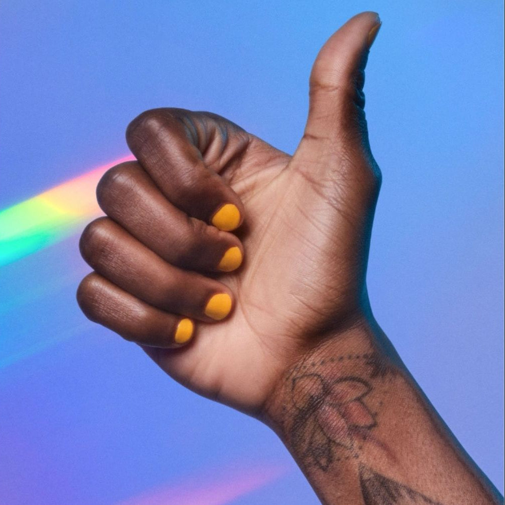 Dark colored hand with thumb up showing orange nail polish on fingers, blue background.