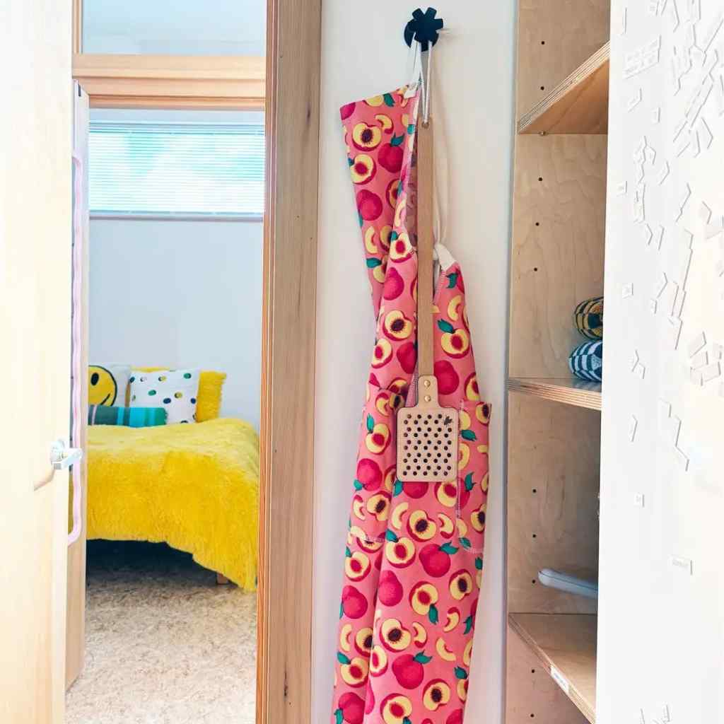 Colorful apron with floral pattern hanging on a hook in a room with a bed and shelves.