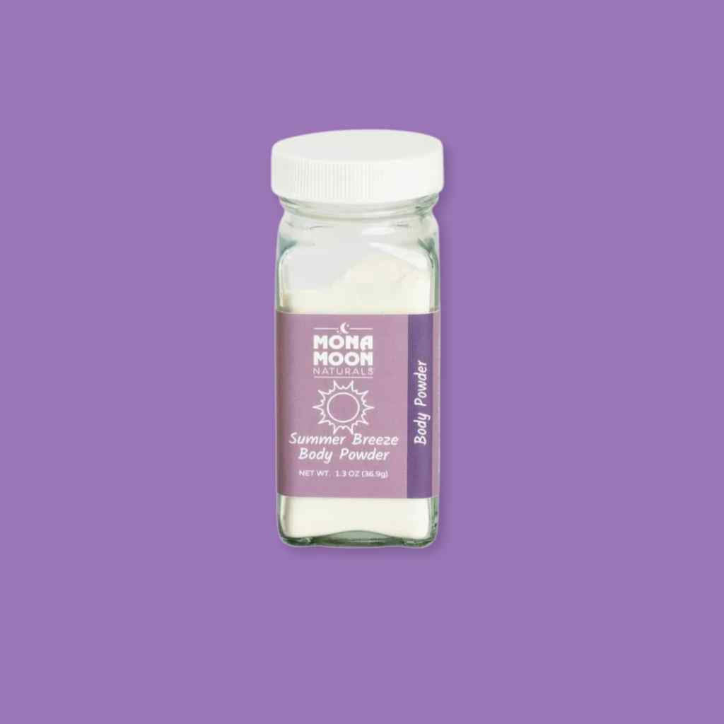 Glass jar of talc-free Mona Moon Summer Breeze body powder with a purple label on a purple background