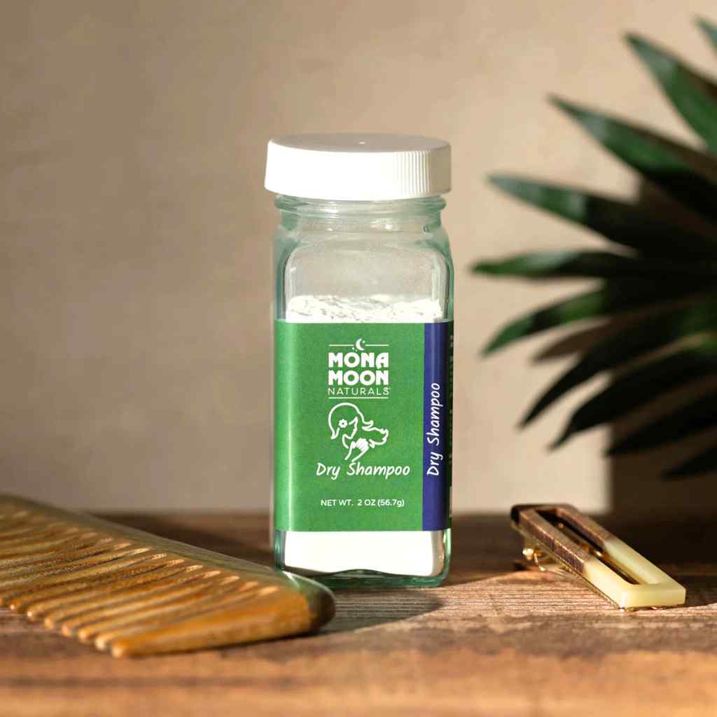 Mona Moon Naturals dry shampoo bottle on a wooden surface with a comb and brush in the background.