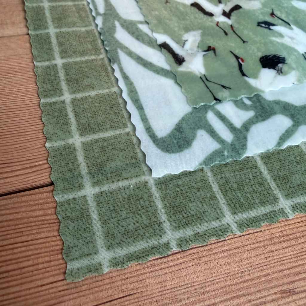 Close up of beeswax wrap, three patterns in green on wood surface.