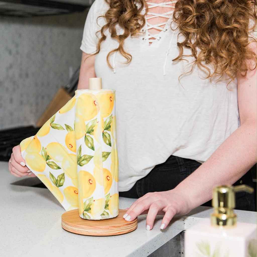 A person holding a vintage lemon print reusable towel roll, with a wooden holder in the background.