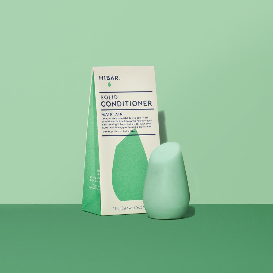 3.2 oz mint green conditioner bar, displayed in front of packaging on light green backdrop and dark green tabletop. shape of resembles and tapered, bulb like cylinder with flat, angled top