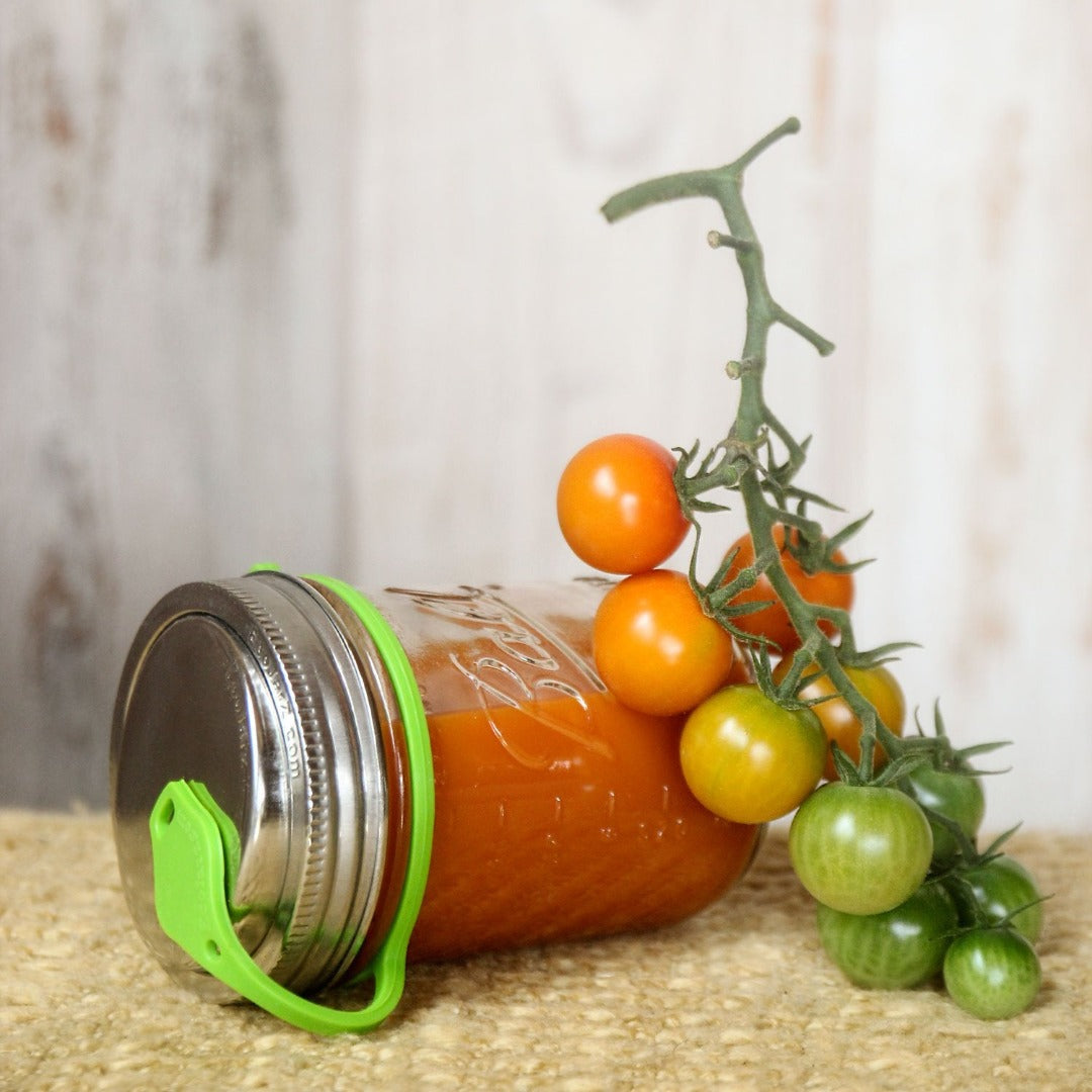 cherry tomatos on vine resting against mason jar filled with tomatoe juice on its side, includes eco jarz lid with green pop top
