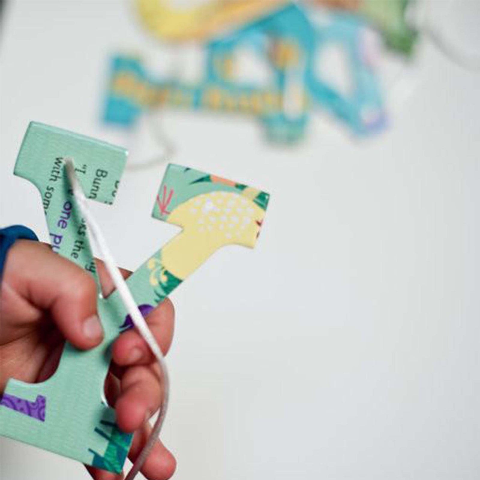 Childs hand holding a green and multicolored unique design of the letter "Y" with white ribbon