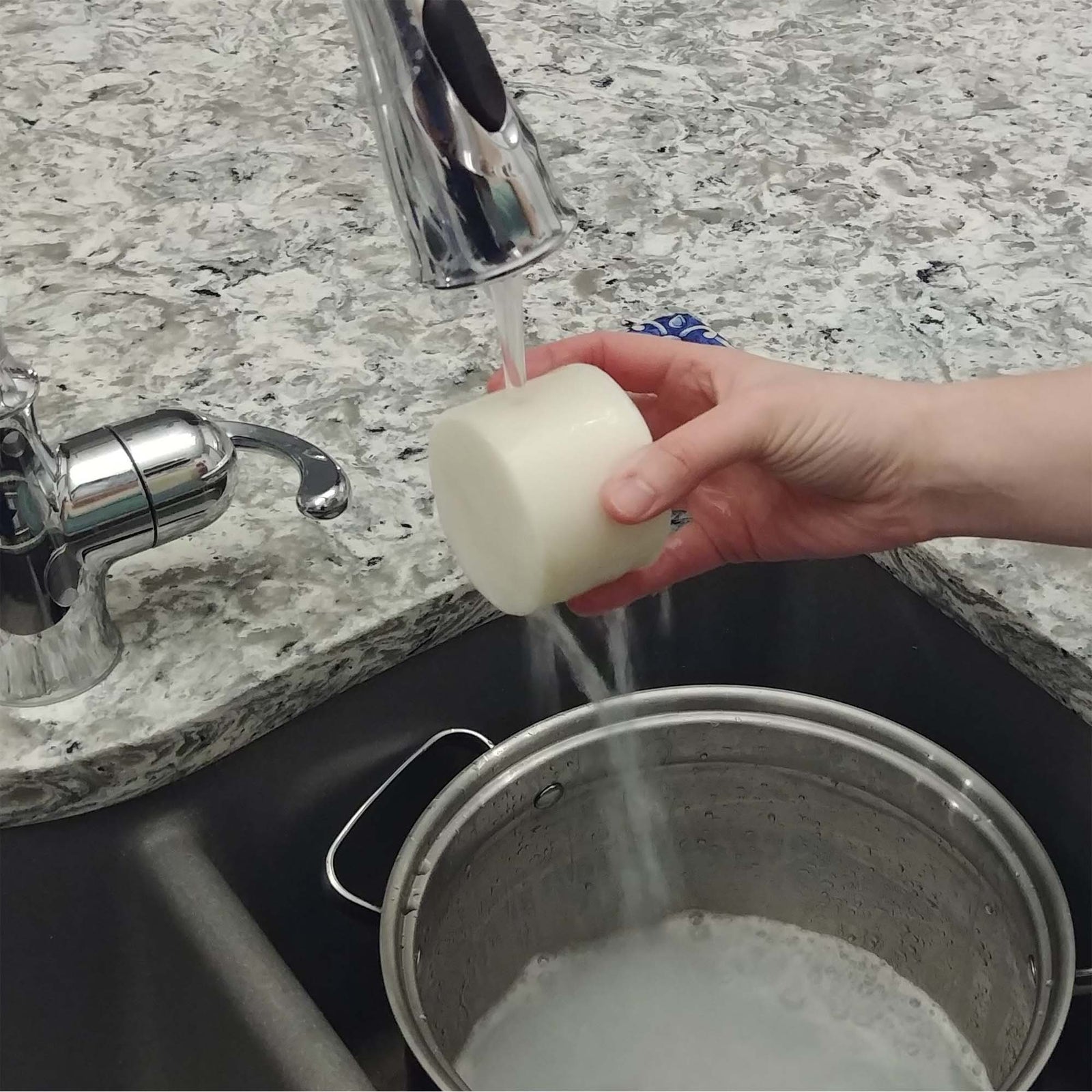 hand holding 7 oz dish soap cylinder under running water in sink, cleaning silver pot