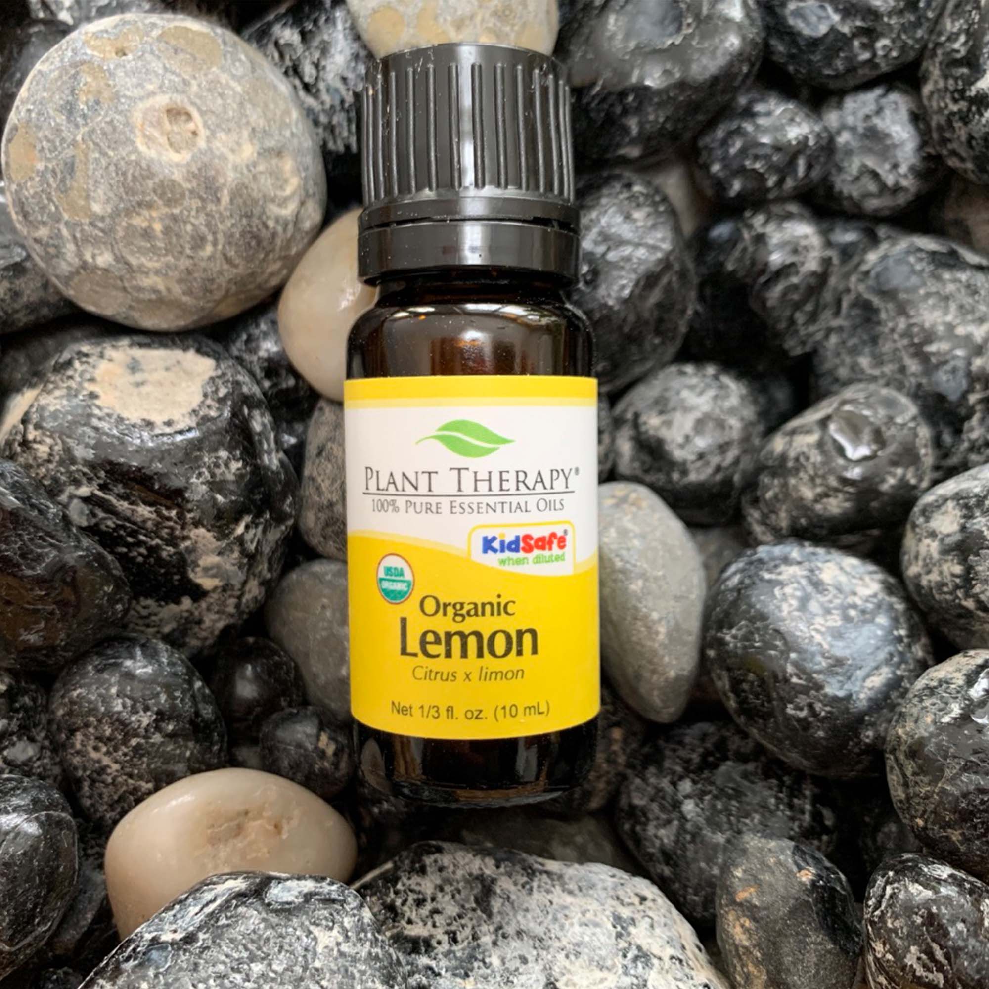 black bottle with yellow label. organic lemon essential oil blend, displayed on assorted rocks. 10 ml