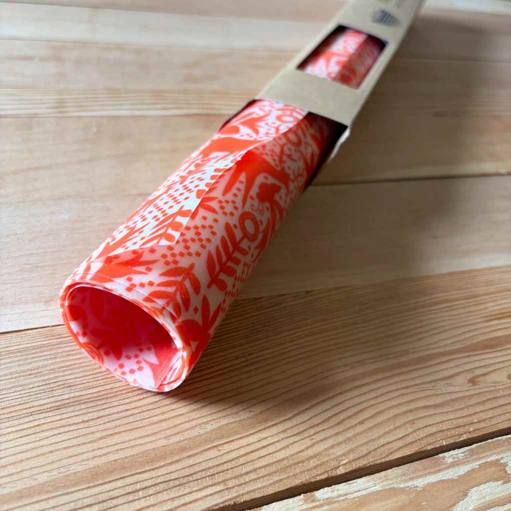 A roll of red and white patterned wrapping paper partially unrolled from its cardboard packaging, resting on a light-colored wooden surface.