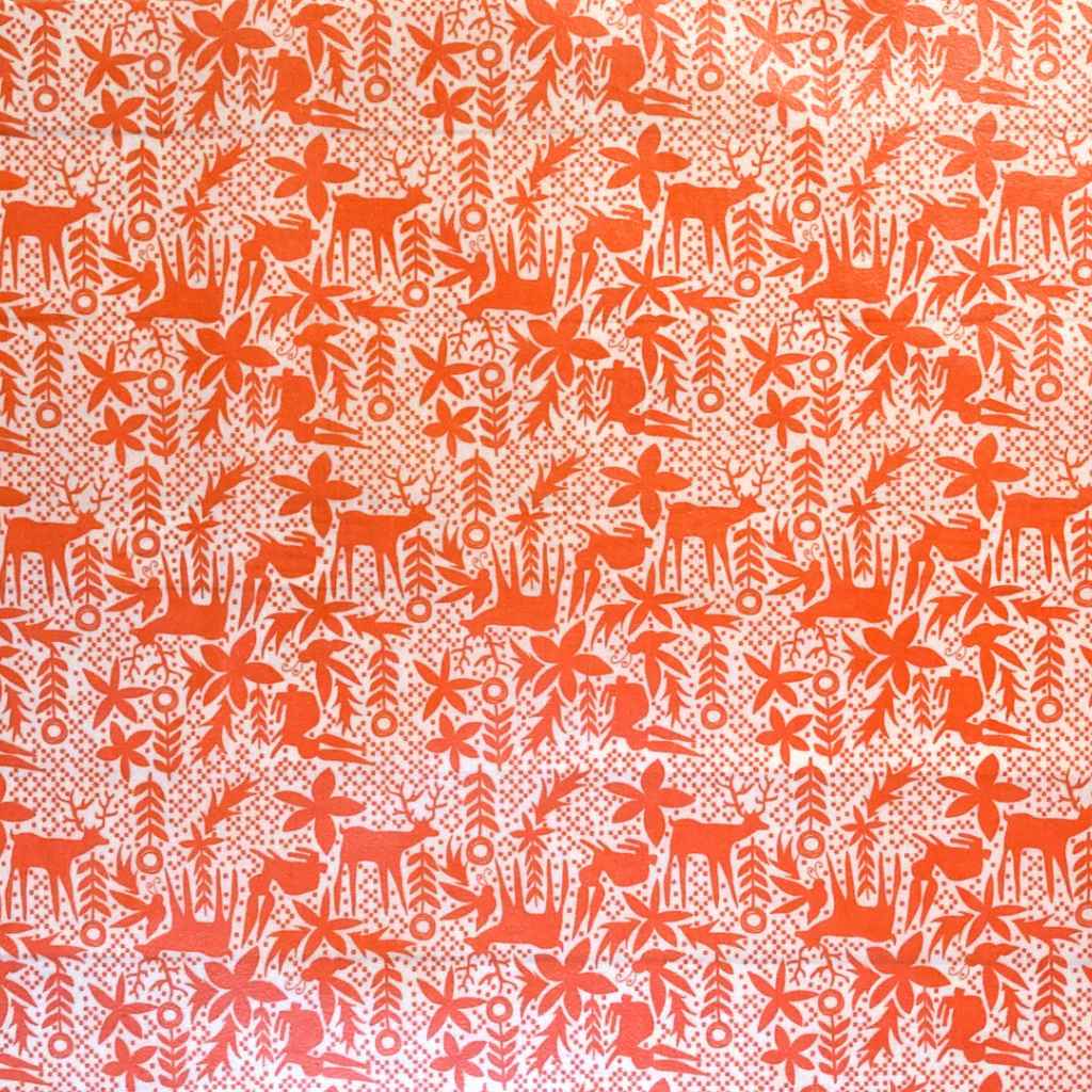 A close-up of a beeswax fabric or wallpaper featuring orange stylized deer, trees, and floral motifs on a white background.