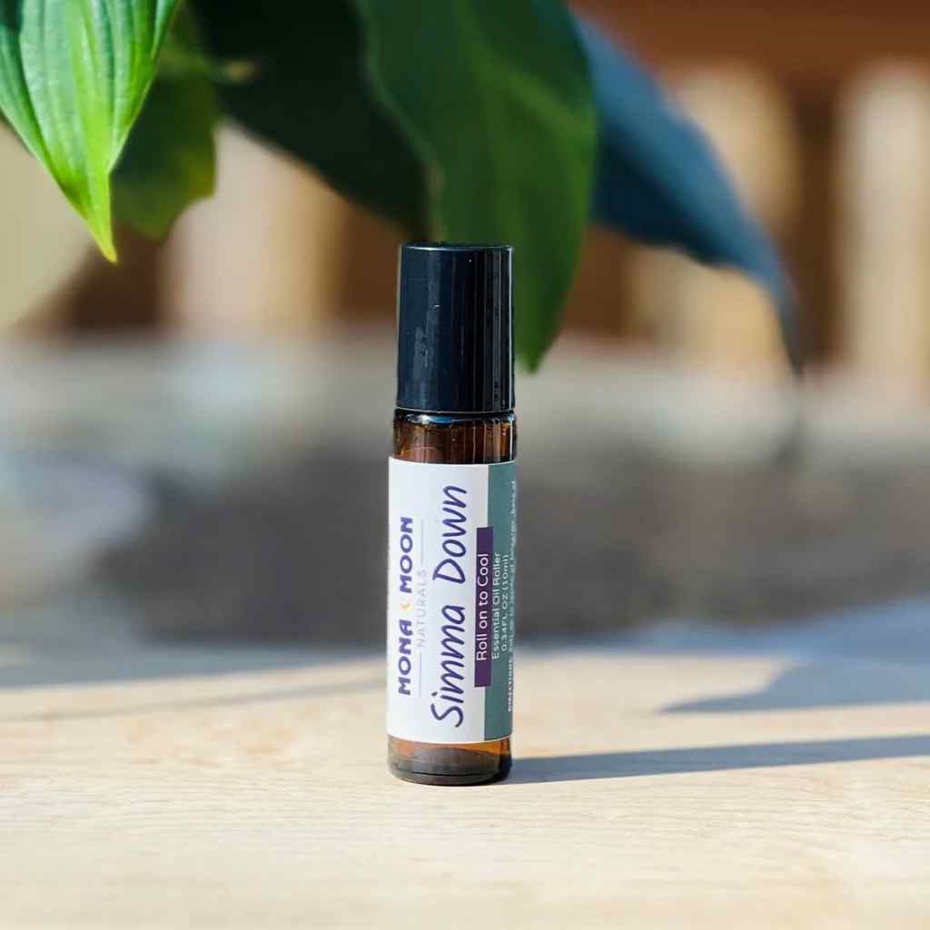 Roll-on bottle labeled 'Simma Down' by Mona Moon on a wooden surface with green leaves in the background.