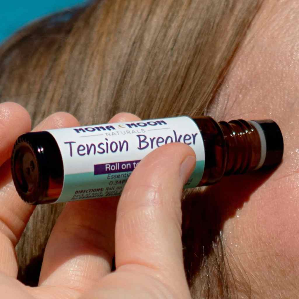 Roll-on bottle labeled 'Tension Breaker' held against skin with blurred background