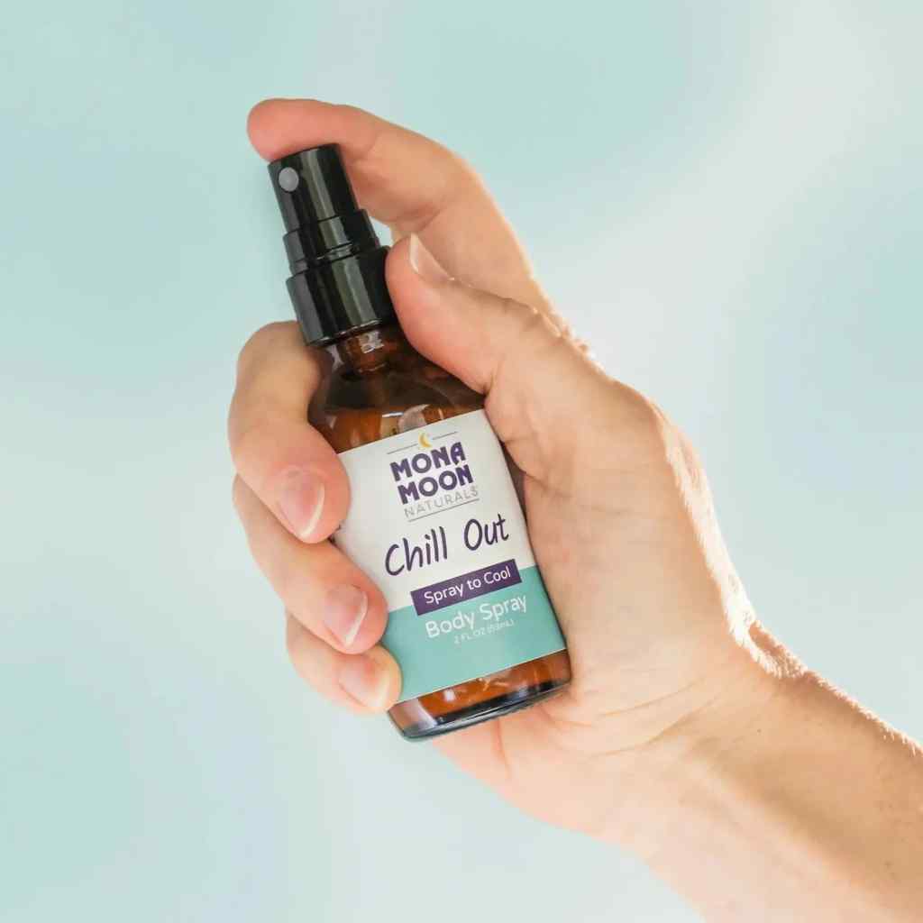 Hand holding a bottle of Mona Moon 'Chill Out' body spray against a light blue background
