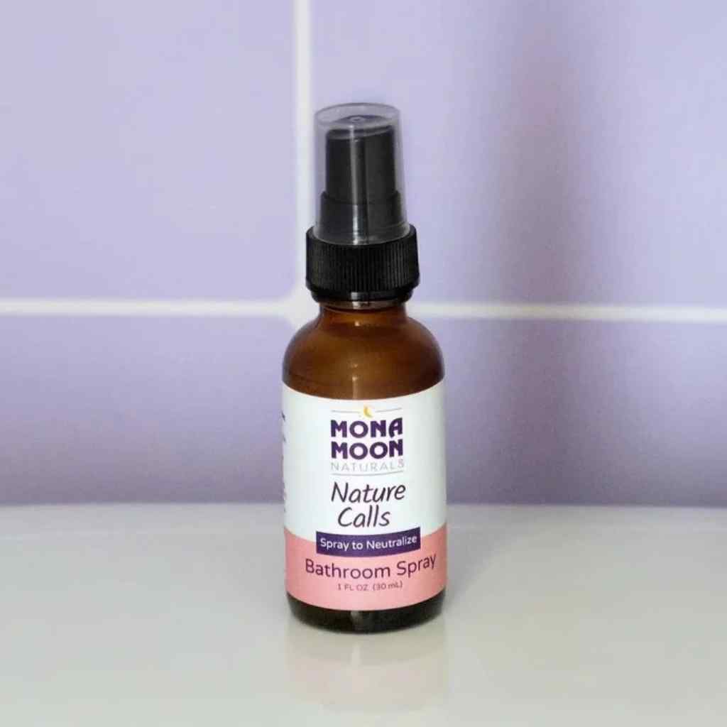 Bottle of Mona Moon Nature Calls Bathroom Spray on a white surface with a purple tiled wall background