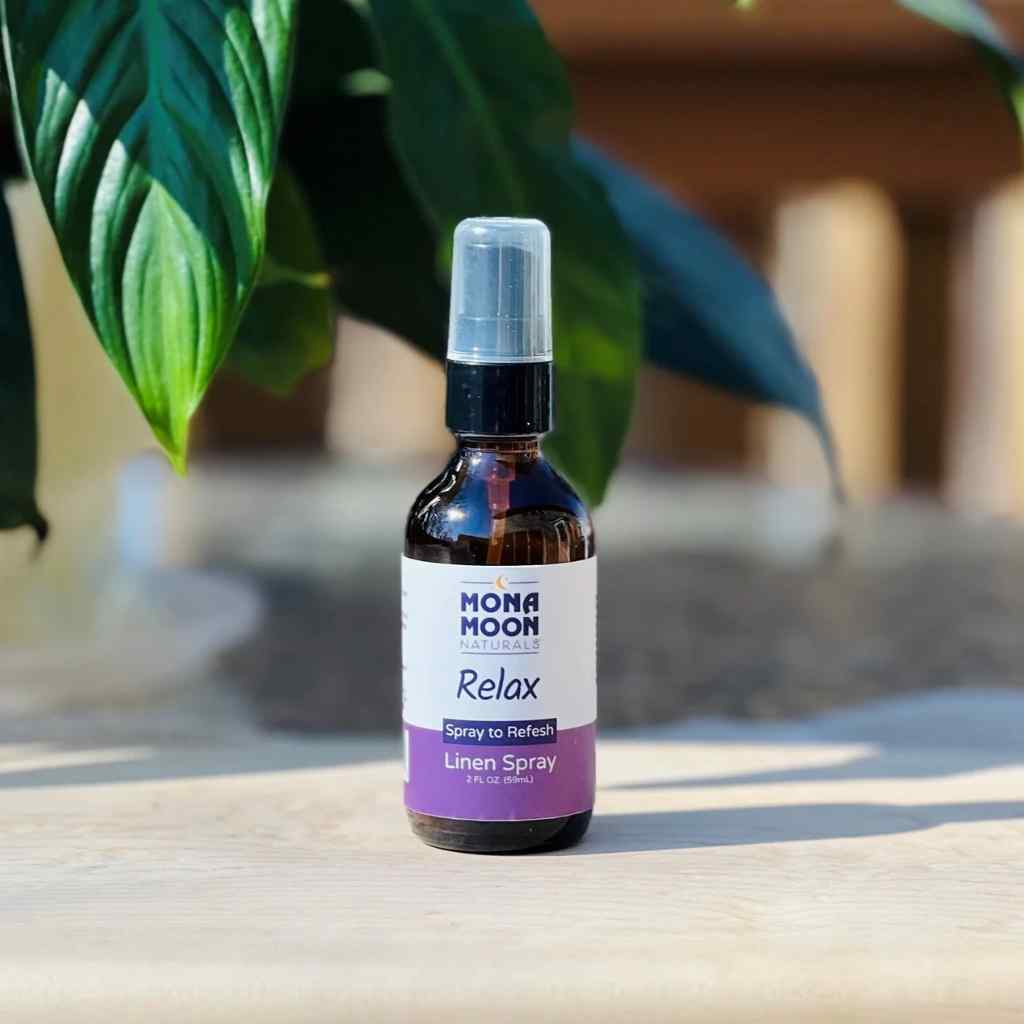 Mona Moon Relax linen spray bottle on a wooden surface with green leaves in the background