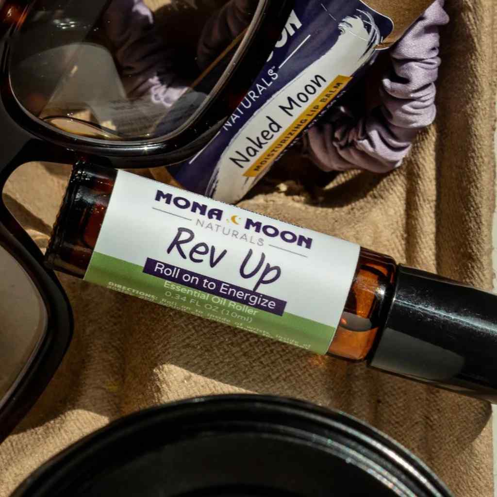 Mona Moon Naturals 'Rev Up' roll-on bottle on a textured surface with a blurred background.