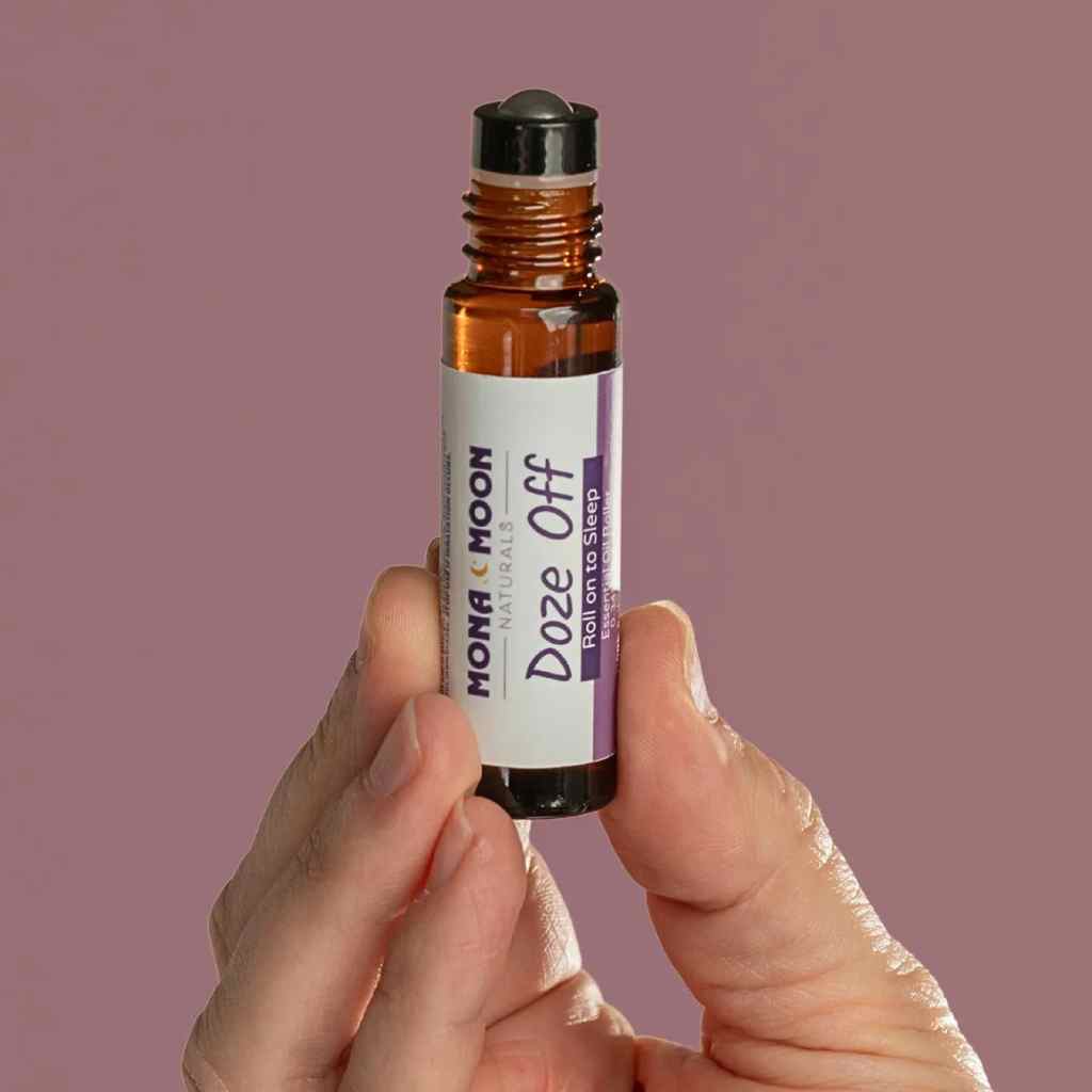 Hand holding a bottle of Mona &amp; Moon 'Doze Off' rollerball against a purple background