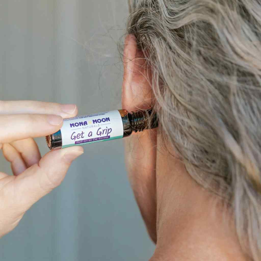 Person holding a roll-on bottle labeled 'Get a Grip' by Mona Moon against a neutral background.