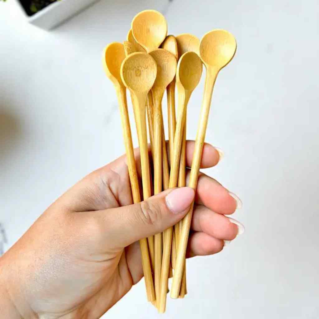 hand holding long wooden spoons on grey background.