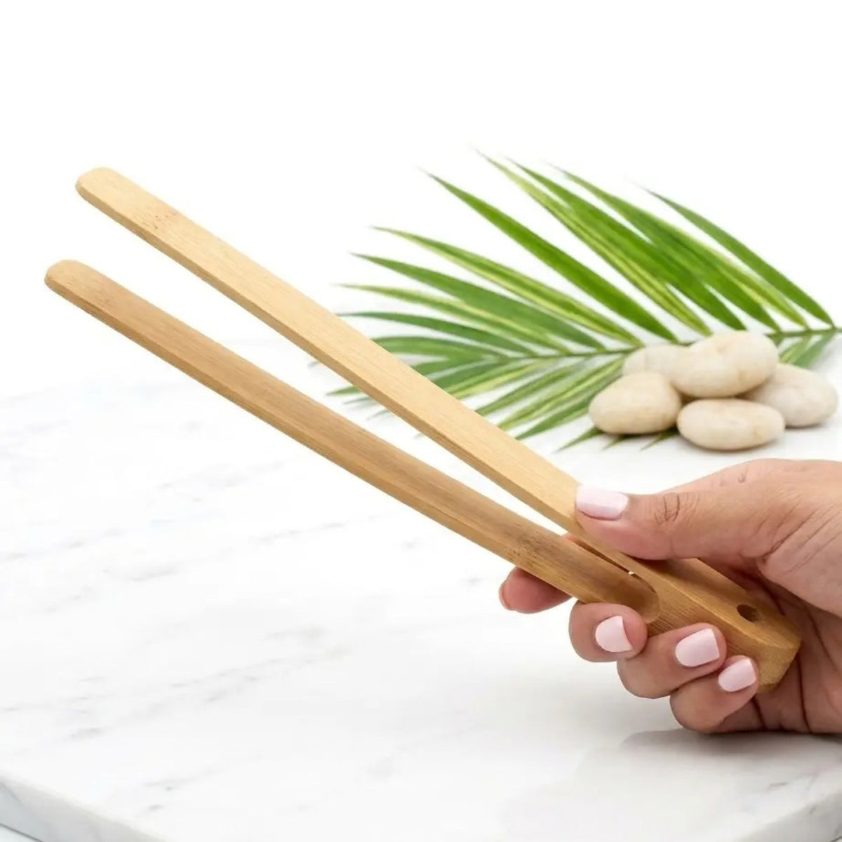wood tongs in hand with white background, white stones and a plant leaf