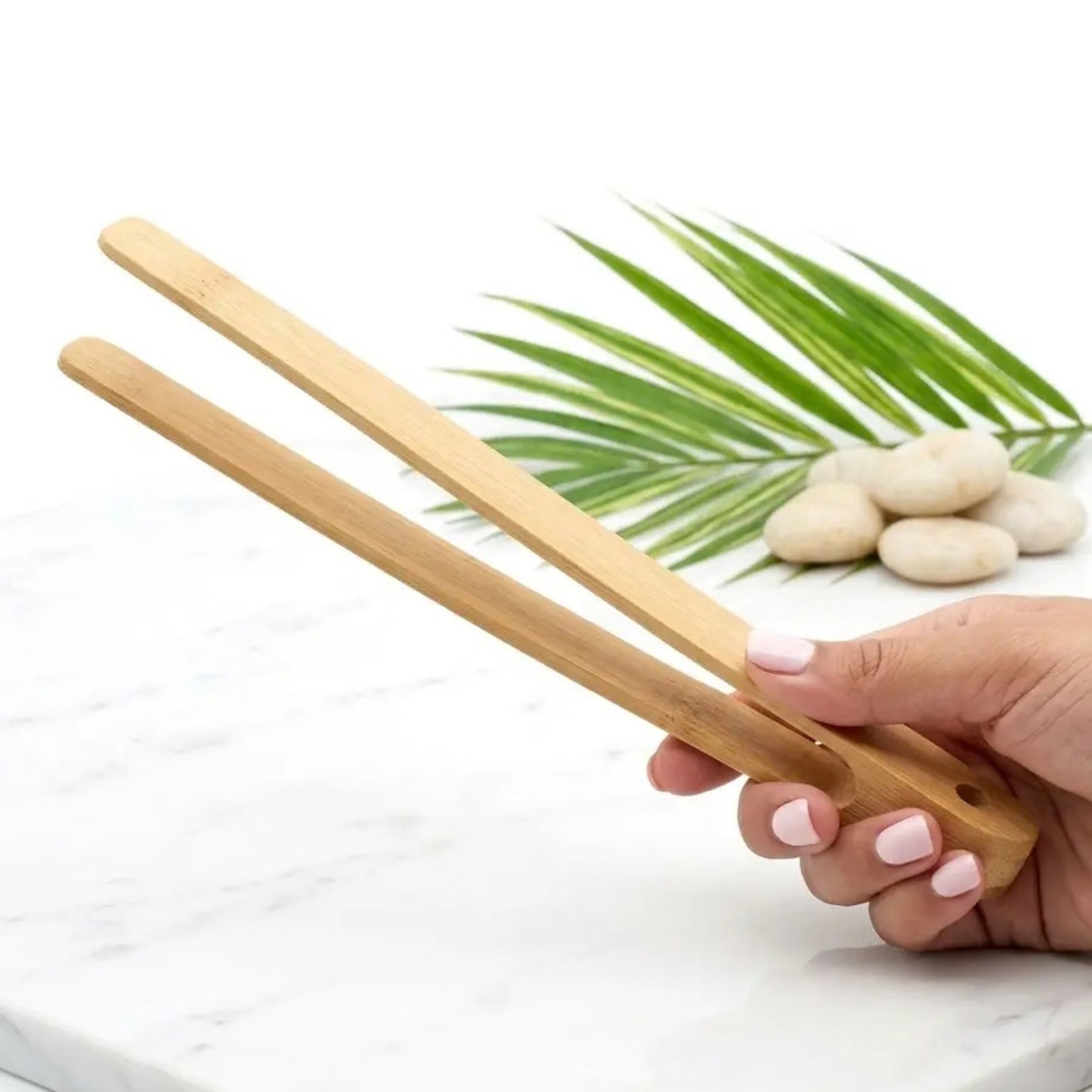 wood tongs in hand with white background, white stones and a plant leaf