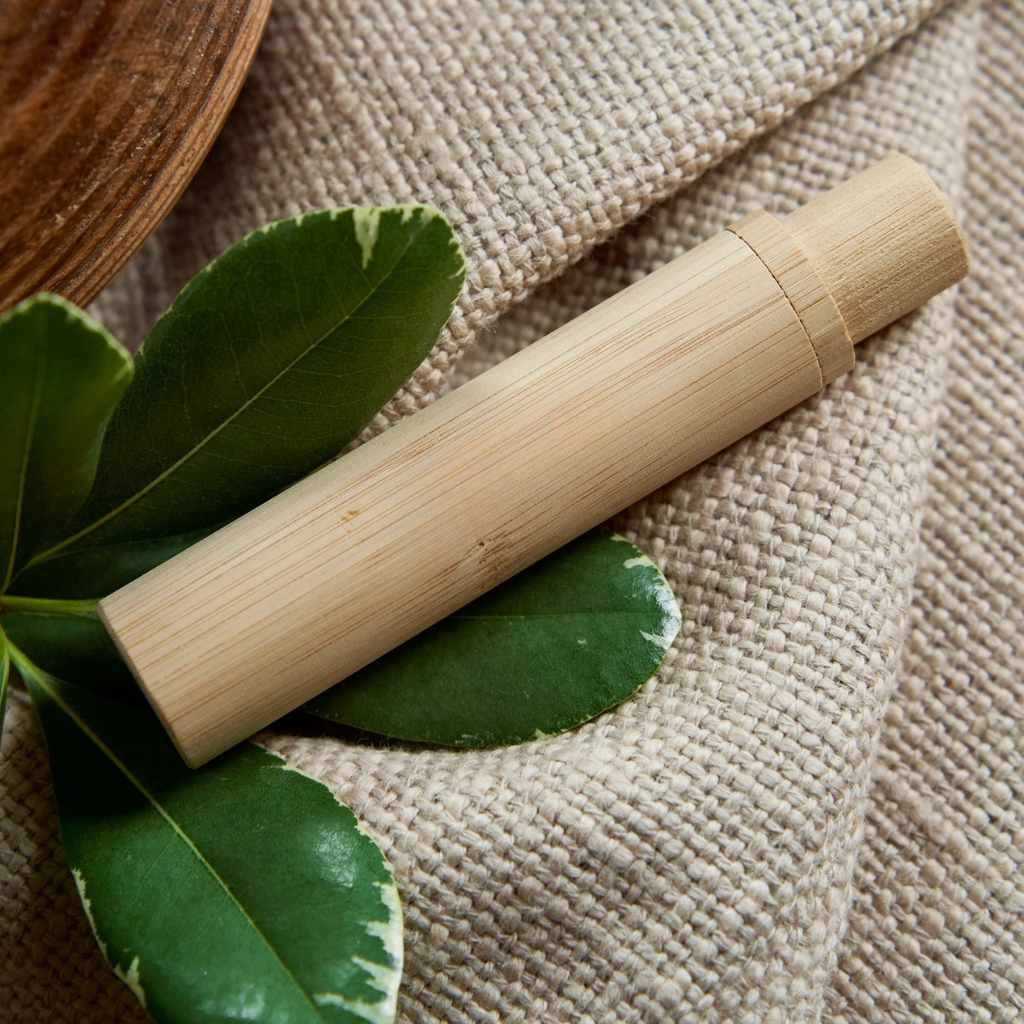 Bamboo toothbrush holder on a textured surface with green leaves