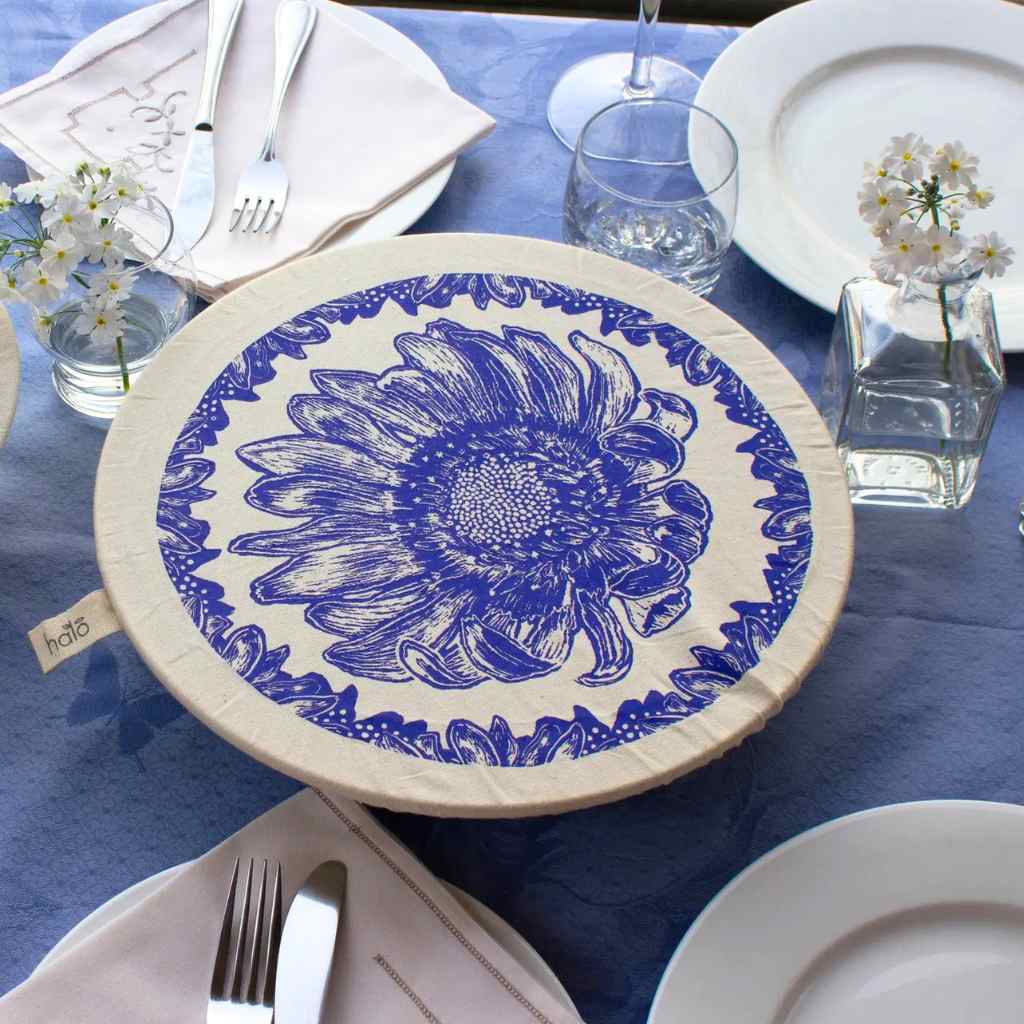 Table setting with a blue floral design dish cover and white plates on a blue tablecloth.