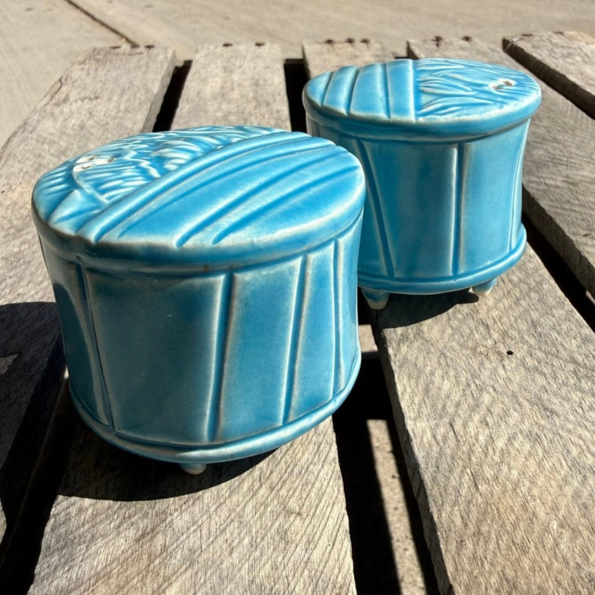 Two small round ceramic salt and pepper shakers with a blue/turquoise patterned glaze, displayed on a rustic wooden surface.