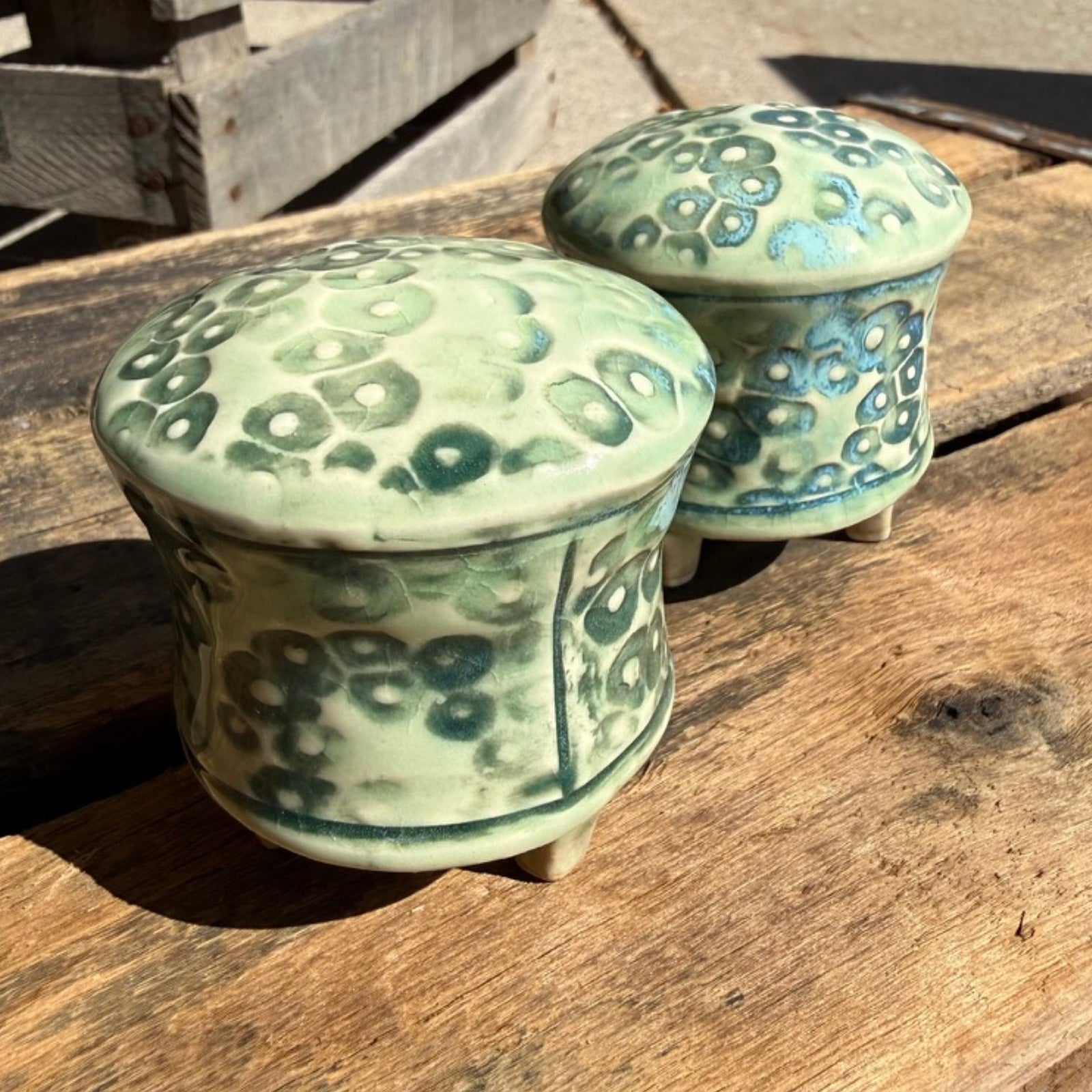 Two small round ceramic salt and pepper shakers with a light green and blue-green patterned glaze, displayed on a rustic wooden surface.