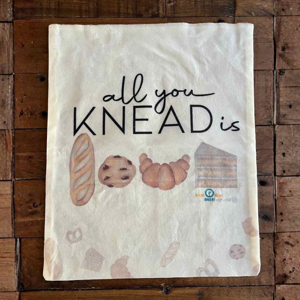 Bread bag front side featuring baked goods on rustic wood background with words, "All you knead is..."