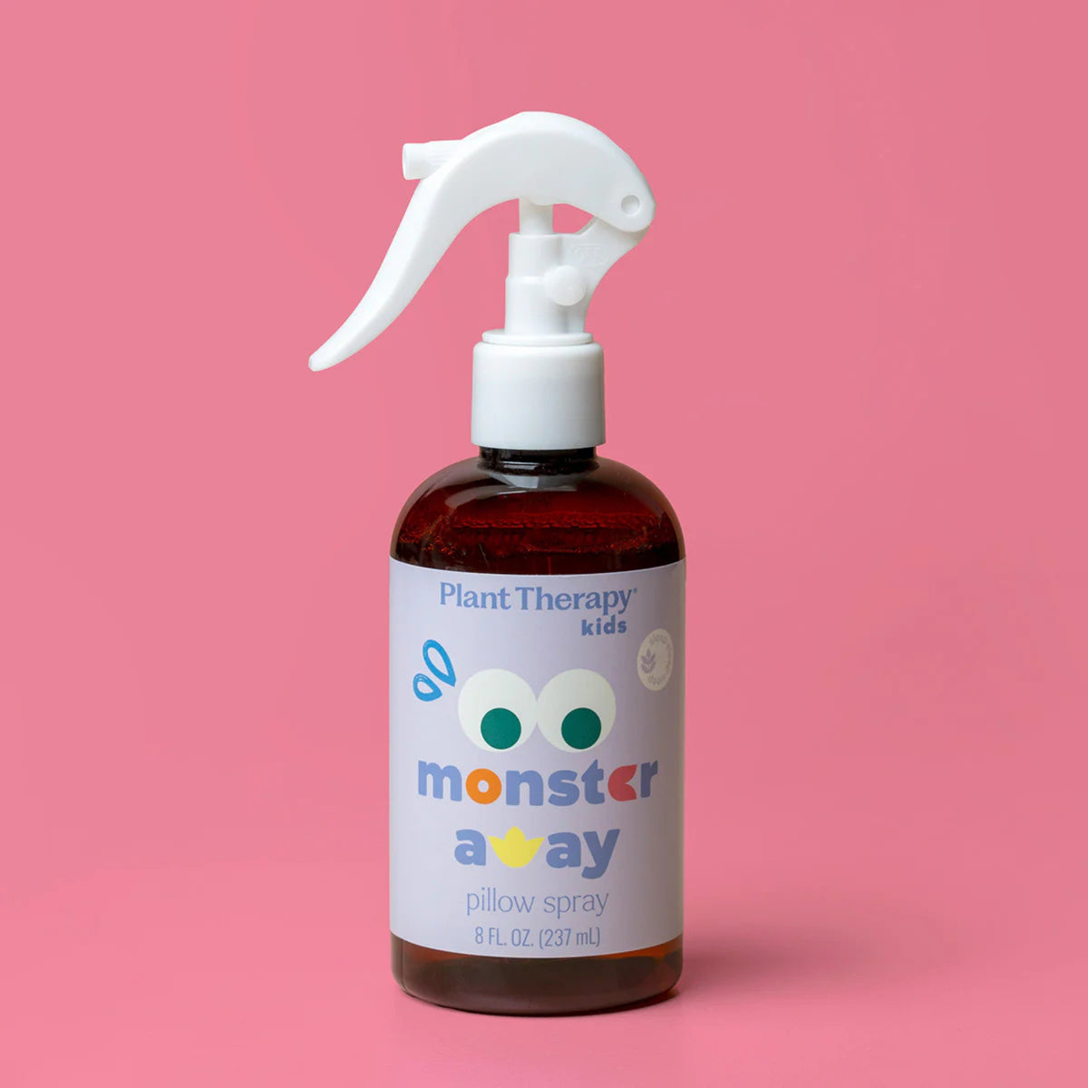 Plant Therapy Kids 'monster away' pillow spray in an amber glass bottle with a white trigger spray top, set against a solid pink background.