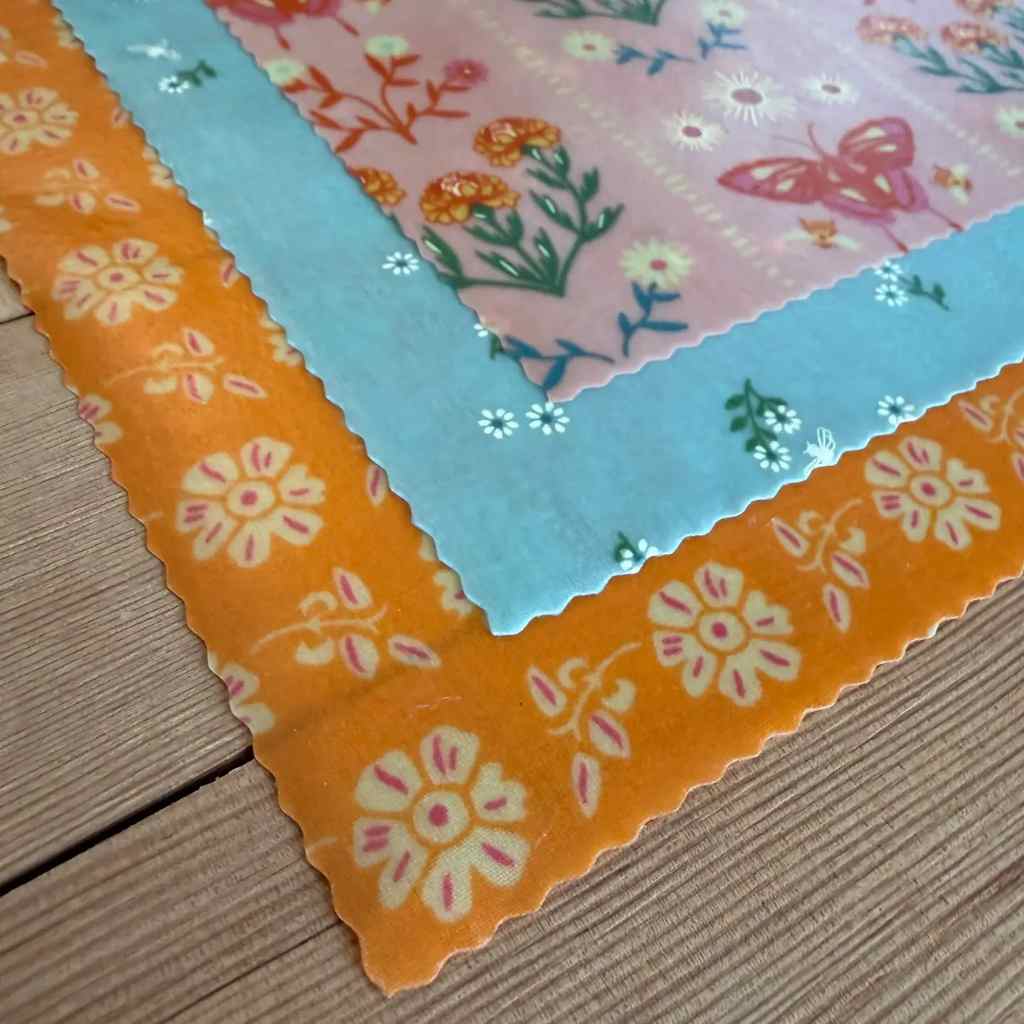 Three colorful beeswax fabric squares with floral patterns on a wooden surface