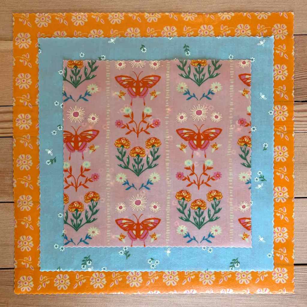 3 sizes of beeswax wrap with butterfly and floral patterns stacked on a wooden background,.