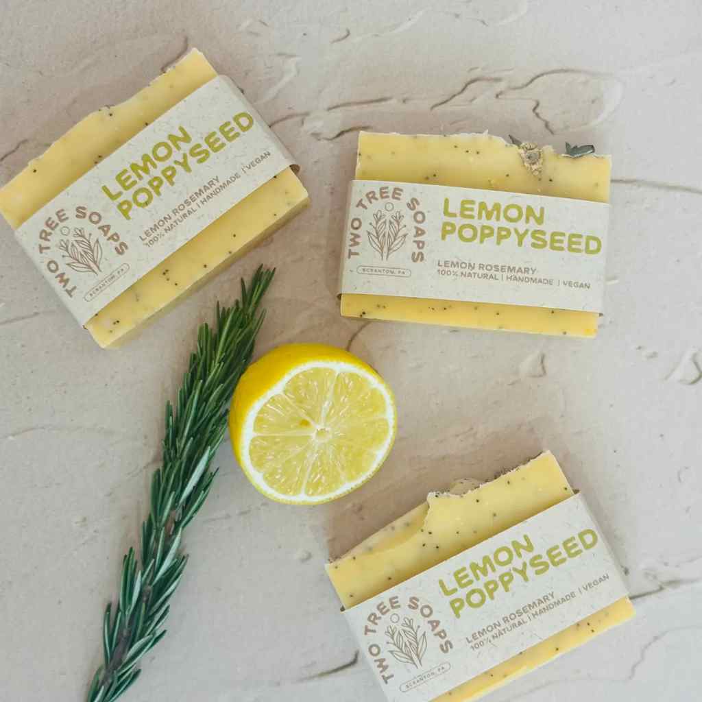 Three bars of lemon poppyseed soap with a lemon and rosemary on a light background