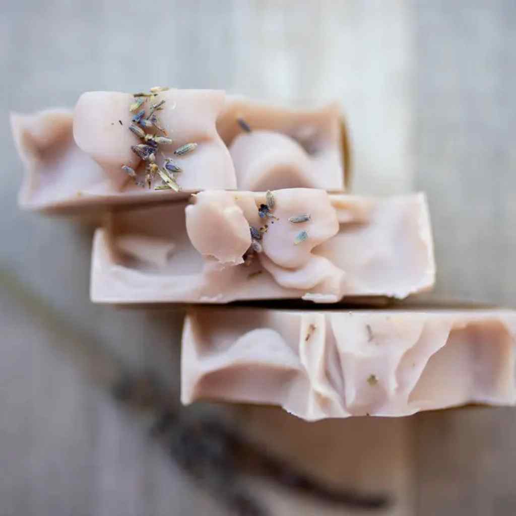 Stack of handmade soap bars with lavender flowers on a wooden surface