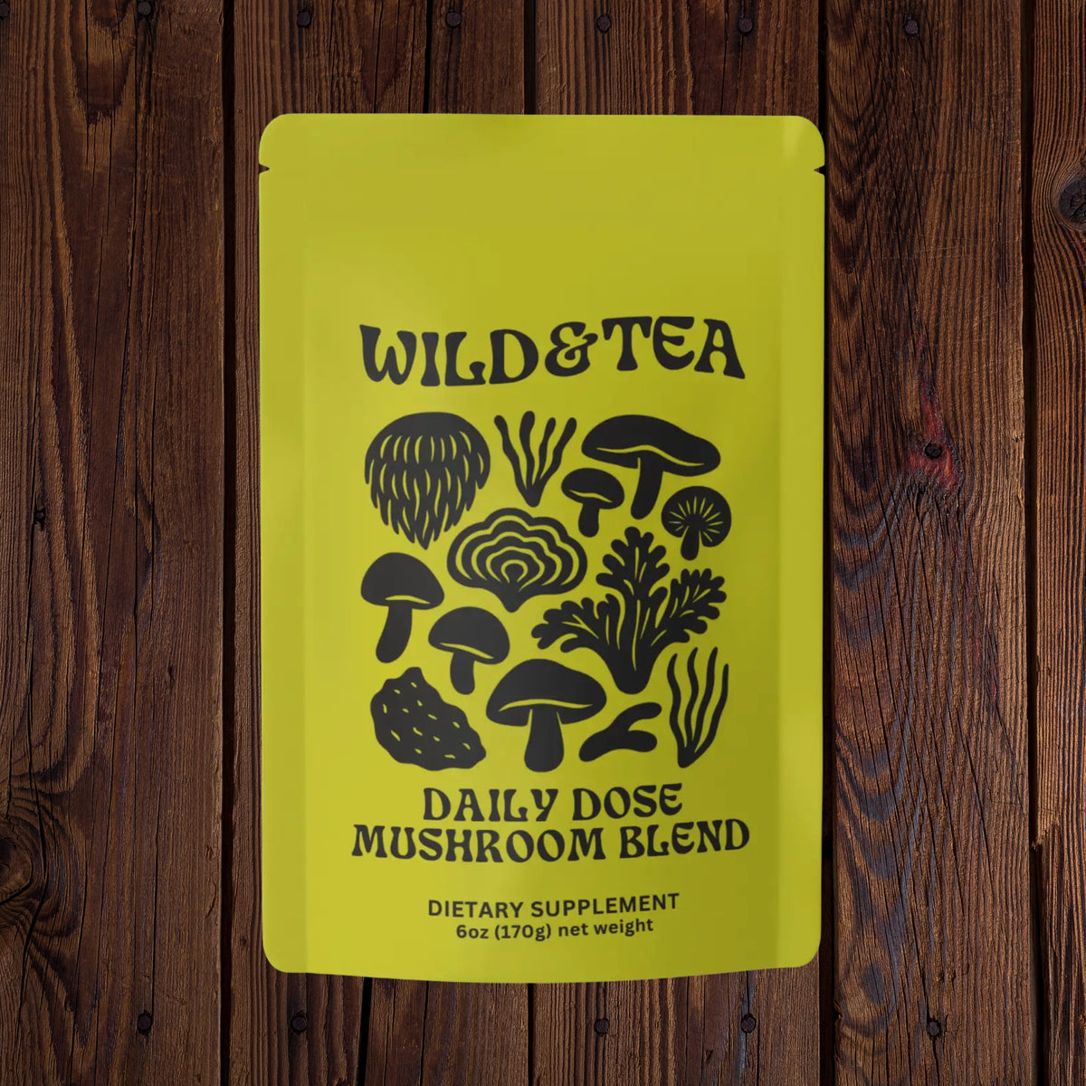 A bright yellow stand-up pouch labeled WILD&amp;TEA Daily Dose Mushroom Blend, photographed flat against a dark brown wood plank background.