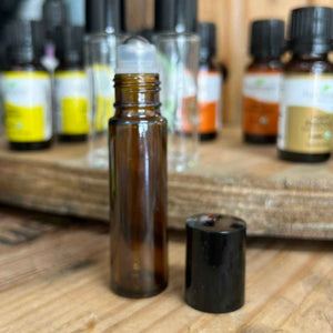 amber colored glass vial for essential oils, shown open, next to black cap. has stainless steel roller ball applicator tip