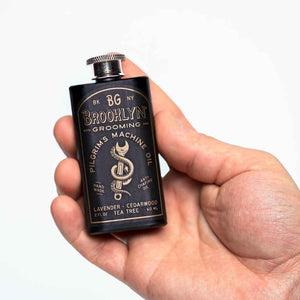 black stainless steel flask containing Brooklyn Grooming Pilgrim's Machine Oil, shown in a man's hand for size context