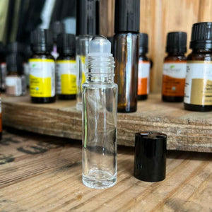 clear glass vial for essential oils, shown open, next to black cap. has stainless steel roller ball applicator tip