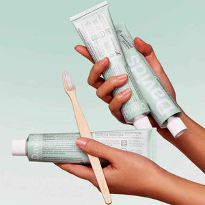 3 tubes of toothpaste and a bamboo toothbrush held by hands Davids Premium Toothpaste 5.25oz in Natural Peppermint