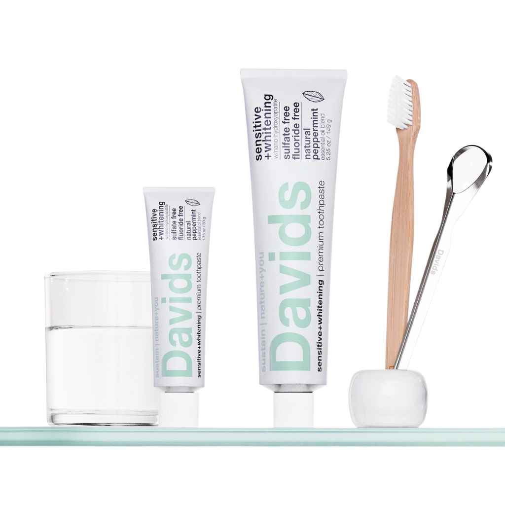 two tubes of toothpaste (one small, one regular sized), a bamboo toothbrush and a glass of water - Davids Premium Toothpaste Sensitive + Whitening in travel size and regular tube