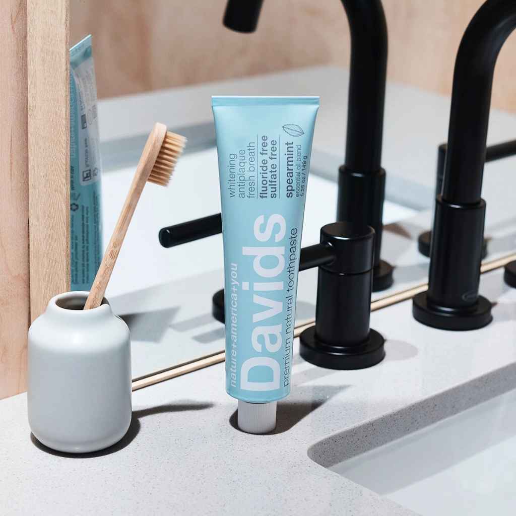Davids Premium Toothpaste 5.25oz in Natural Spearmint shown on bathroom sink next to a bamboo toothbrush