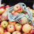 striped natural and blue market string bag full of apples sitting on mound of apples at market