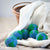 6 wool dryer balls designed to look like the earth in blue and green, shown with a light colored blanket in a basket.. Made by Friendsheep