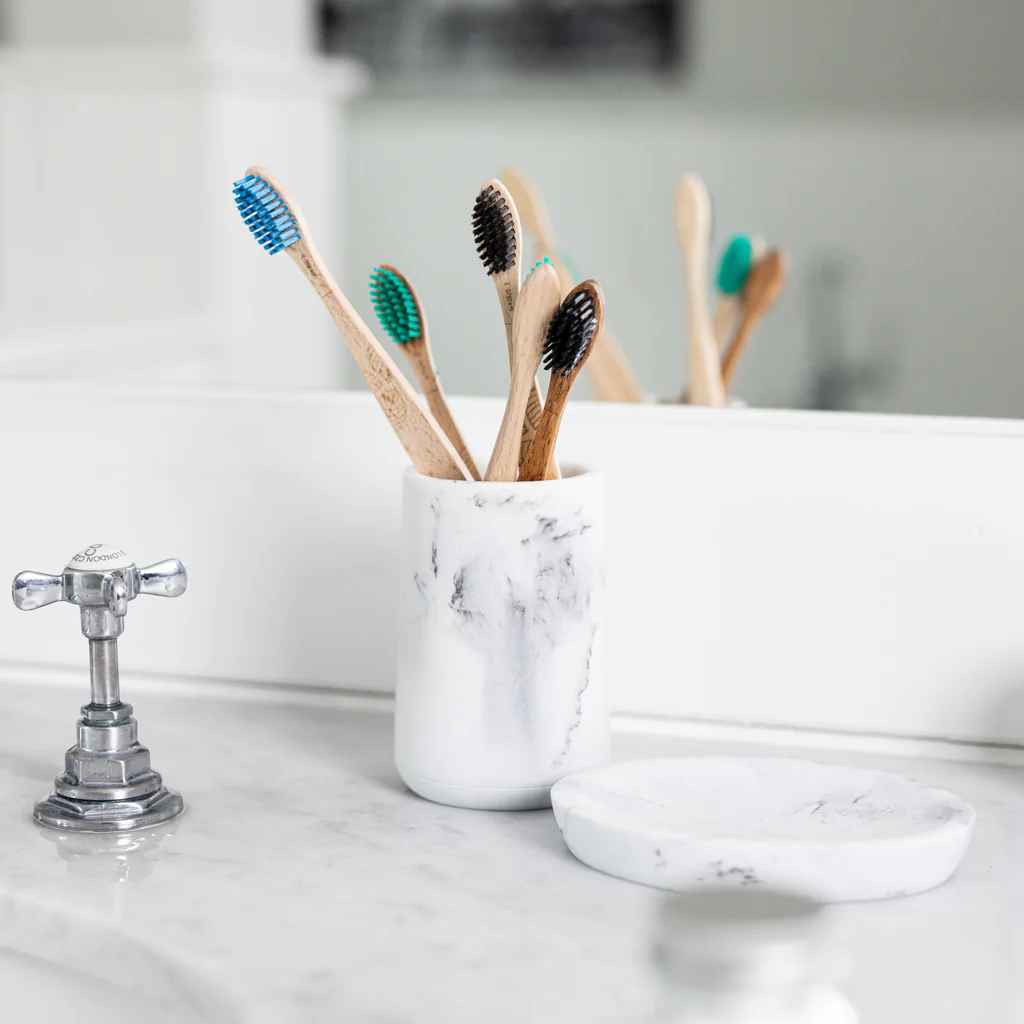 A handful of Georganics beechwood toothbrushes in a stone jar on a bathroom counter.