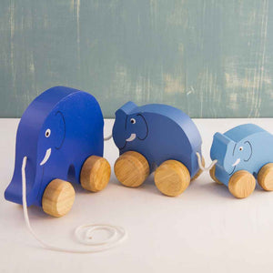 Wooden Pull-Along Toy by Mr. Ellie Pooh shown with three blue elephants in a row. Made of sustainable Albizia wood from Sri Lanka, Fairtrade certified. US compliant coatings.