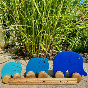 Wooden Pull-Along Toy by Mr. Ellie Pooh shown with three blue elephants in a row. Made of sustainable Albizia wood from Sri Lanka, Fairtrade certified. US compliant coatings.