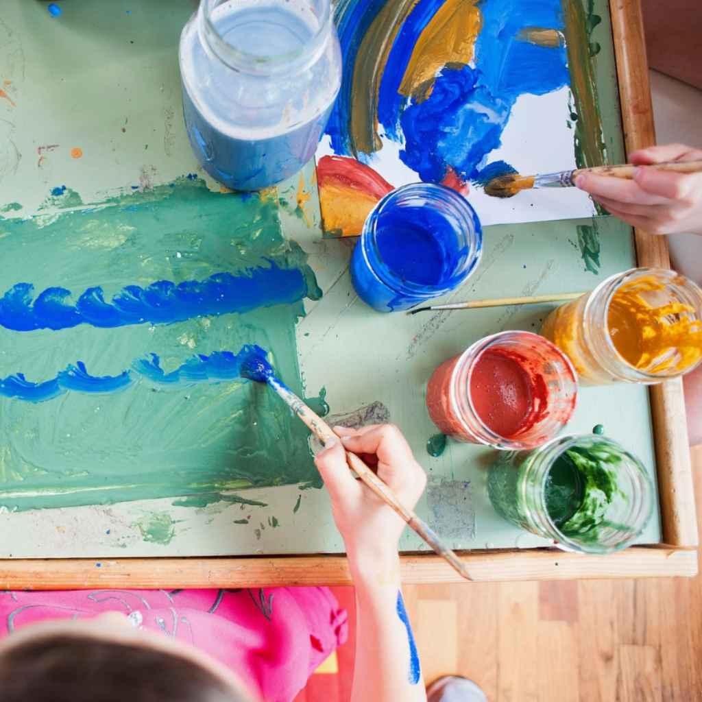 photo taken from above two children using paint brushes to paint