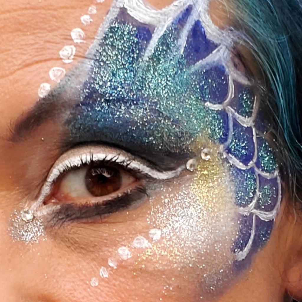 a pilclose up of a woman&#39;s face with blue and white face paint and turquoise  glitter applied. Eco-Friendly Glitter made by Natural Earth Paint