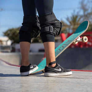 A photo of a skateboarder's legs and feet, wearing a black bamboo bandage on one ankle.